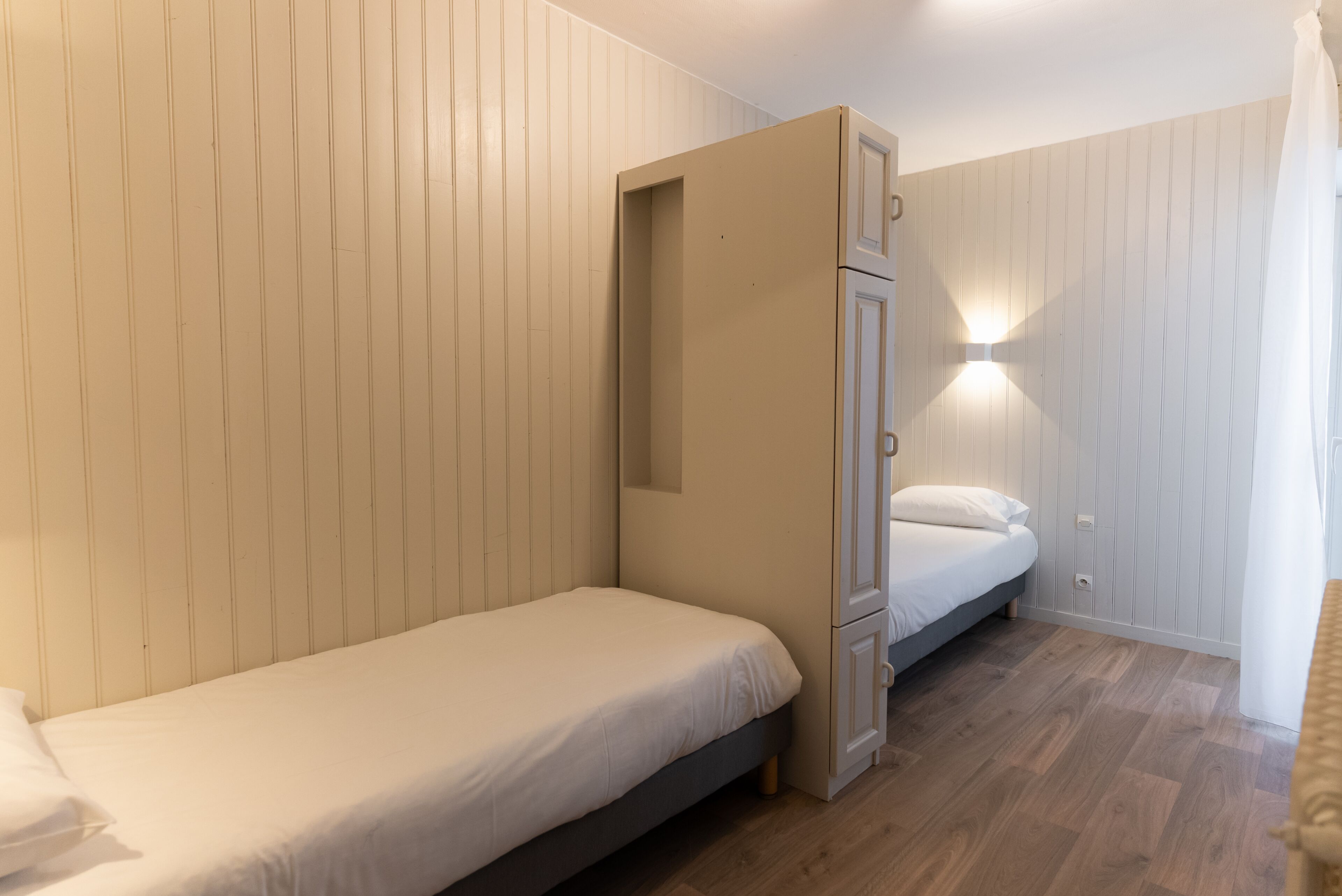A small, compact room with a single bed, a built-in wardrobe, and a wall-mounted light fixture.