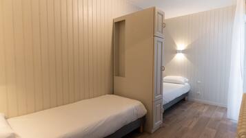 A small, compact room with a single bed, a built-in wardrobe, and a wall-mounted light fixture.