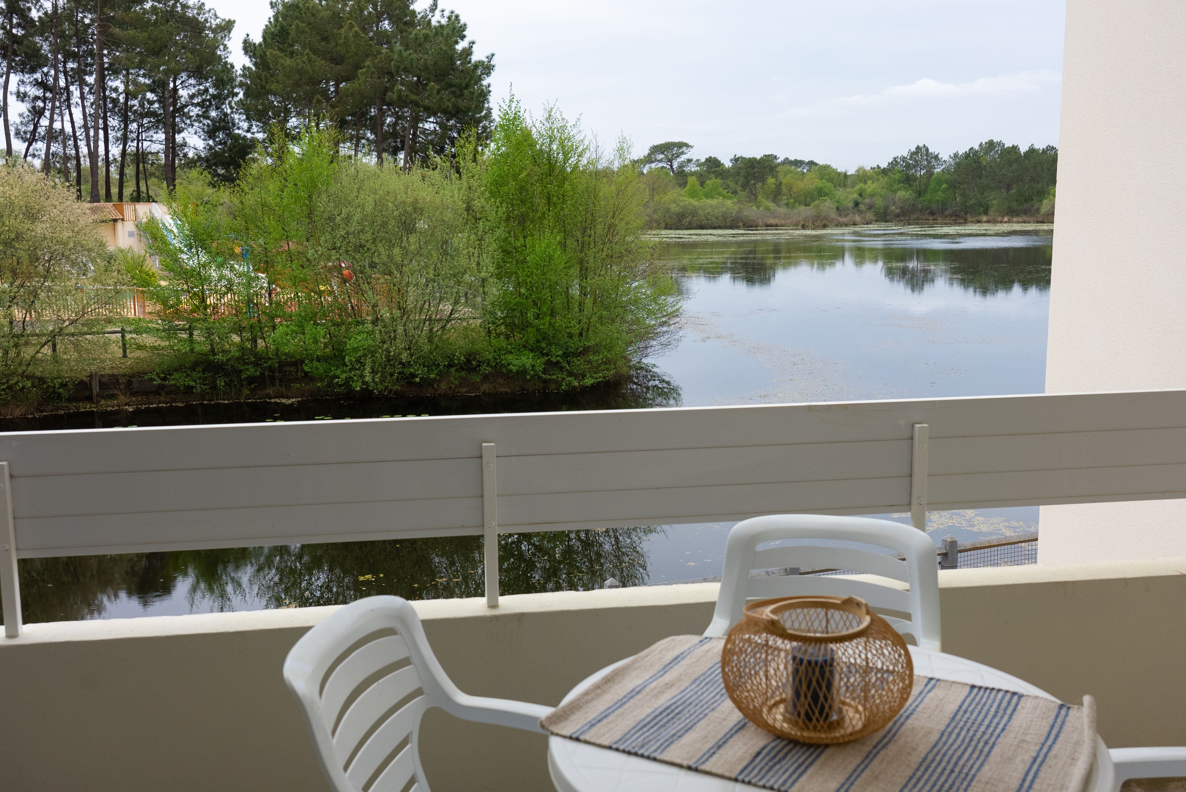 A balcony with a view of a lake, surrounded by greenery and trees.