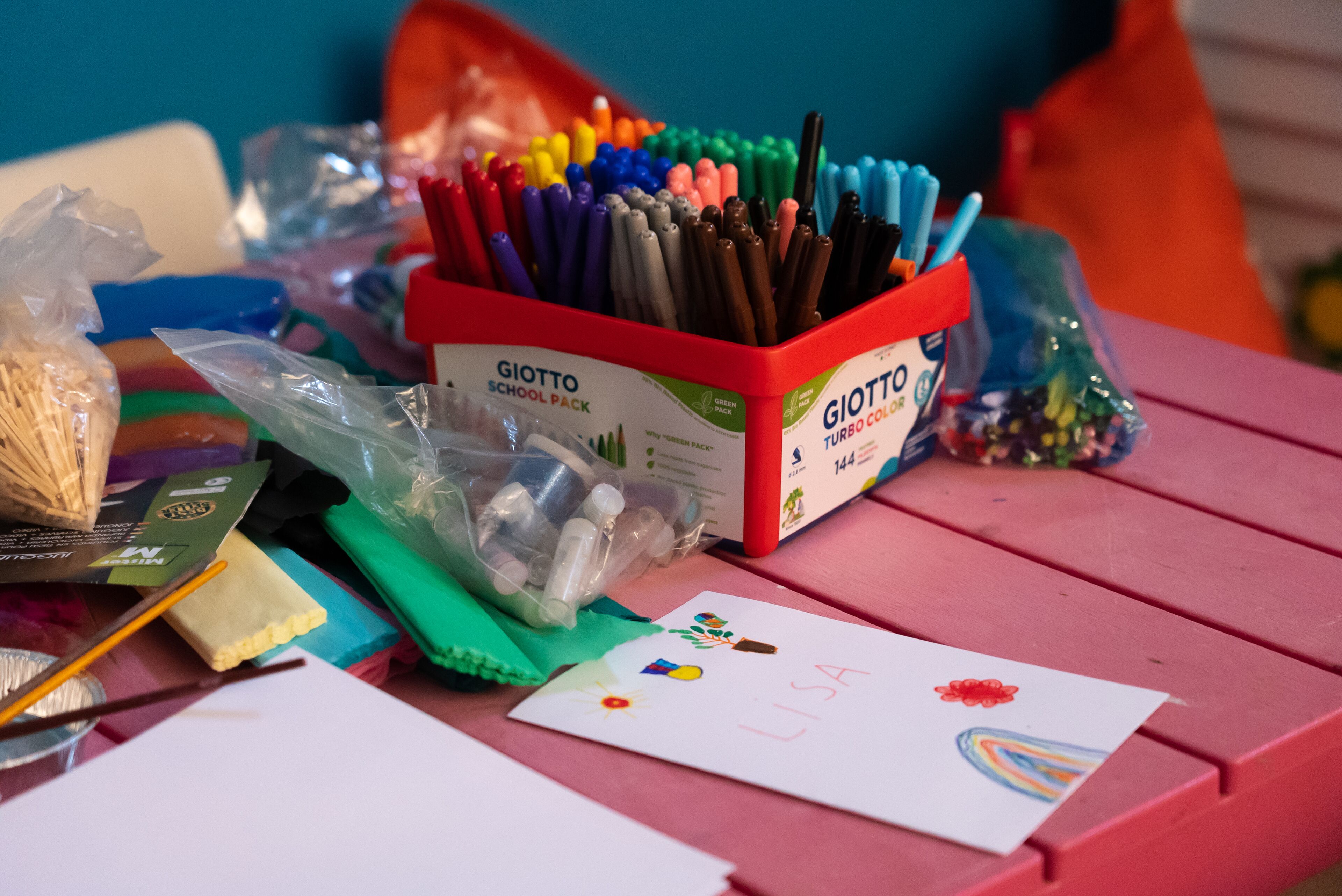 A table with a school pack, markers, and a child's drawing.