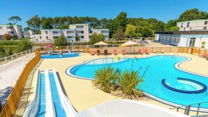 A swimming pool with a slide, surrounded by a fence, and a beach area with umbrellas. - Azureva Lacanau (Lacanau)