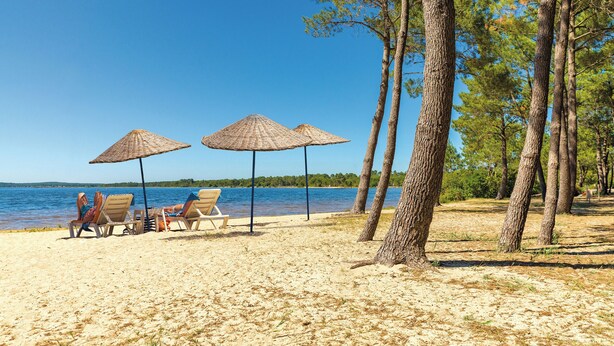 A beach with three umbrellas, lounge chairs, and a view of the water. - Azureva Lacanau (Lacanau)