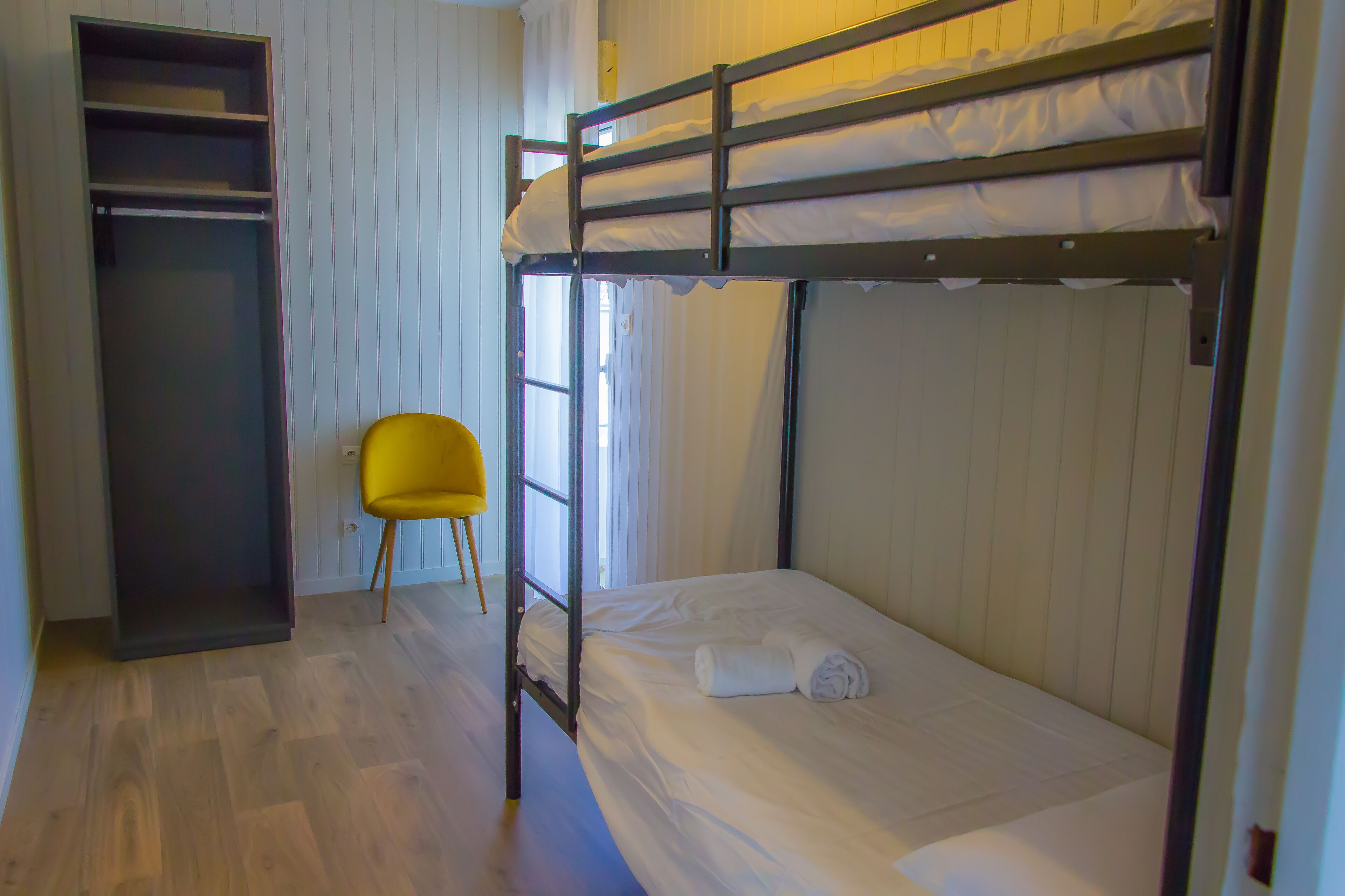 A bunk bed room with a wardrobe and a yellow chair.