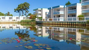 A modern hotel with multiple floors, a reflective water body with lily pads and flowers, and a bridge connecting the buildings. - Azureva Lacanau (Lacanau)