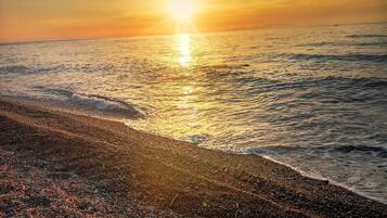 A beach with pebbles and waves at sunset.