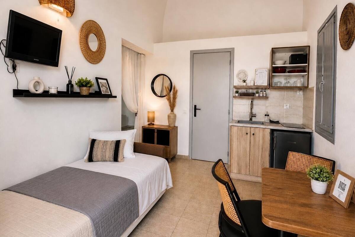 Habitación de hotel compacta con cama, un escritorio pequeño, una mesa de comedor, kitchenette y televisor montado en la pared.