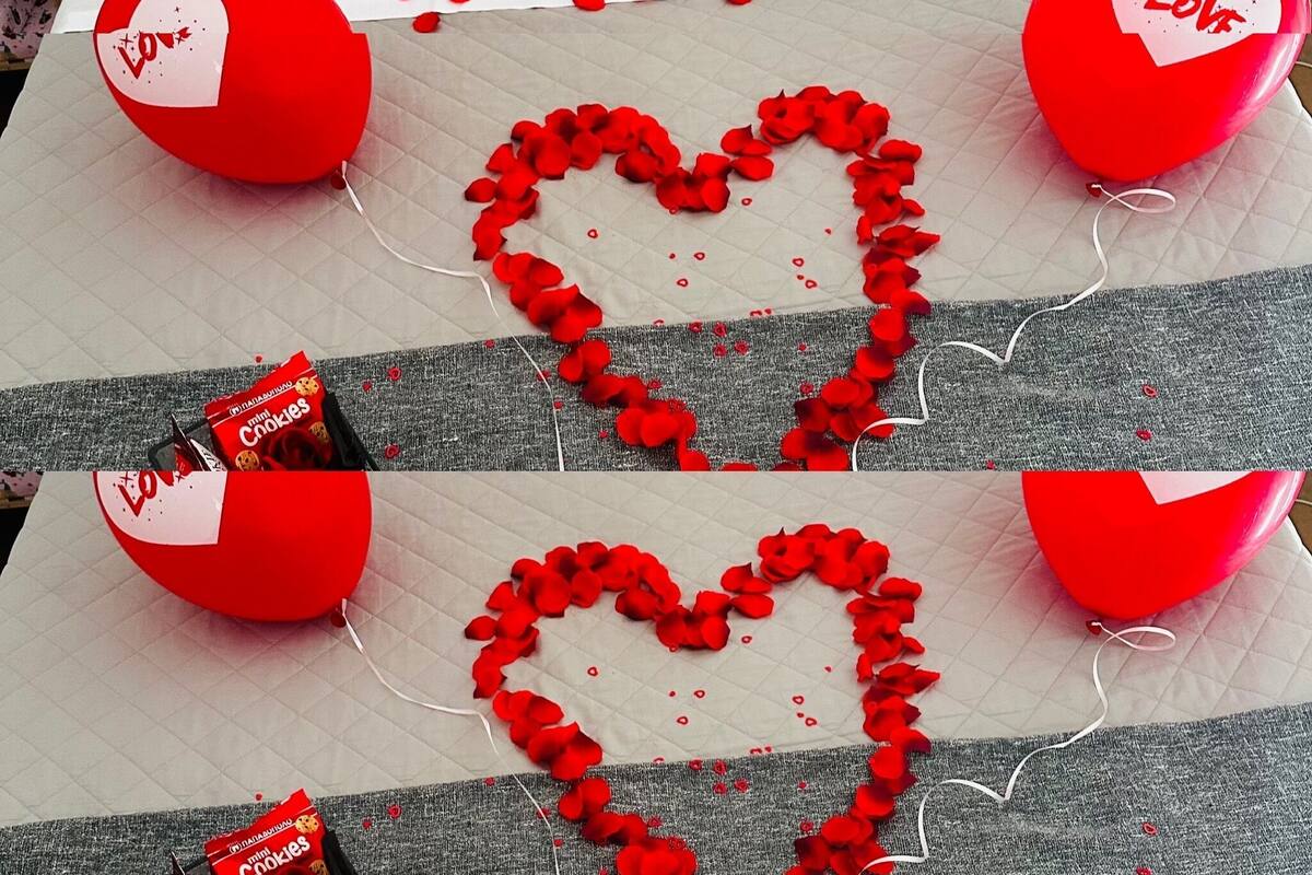 Una cama adornada con globos rojos con forma de corazón y pétalos de rosa dispuestos en un diseño de corazón.