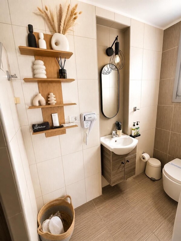 A modern bathroom with a wooden shelf holding toiletries, a white sink, and a toilet. - Mare Nostrum Santo (Santorini)