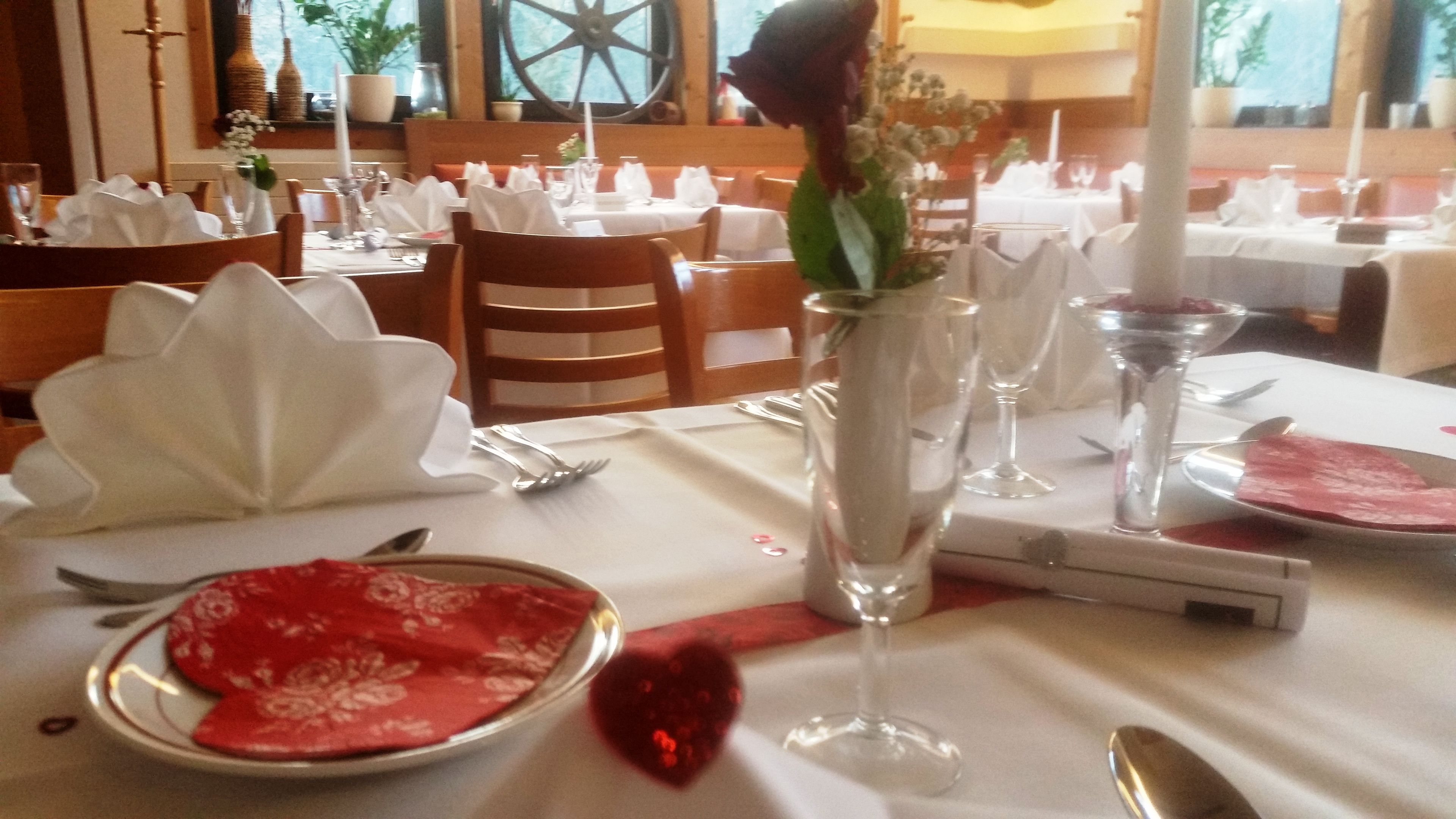 A restaurant setting with tables set for dining, featuring white tablecloths, red napkins, and clear glassware.
