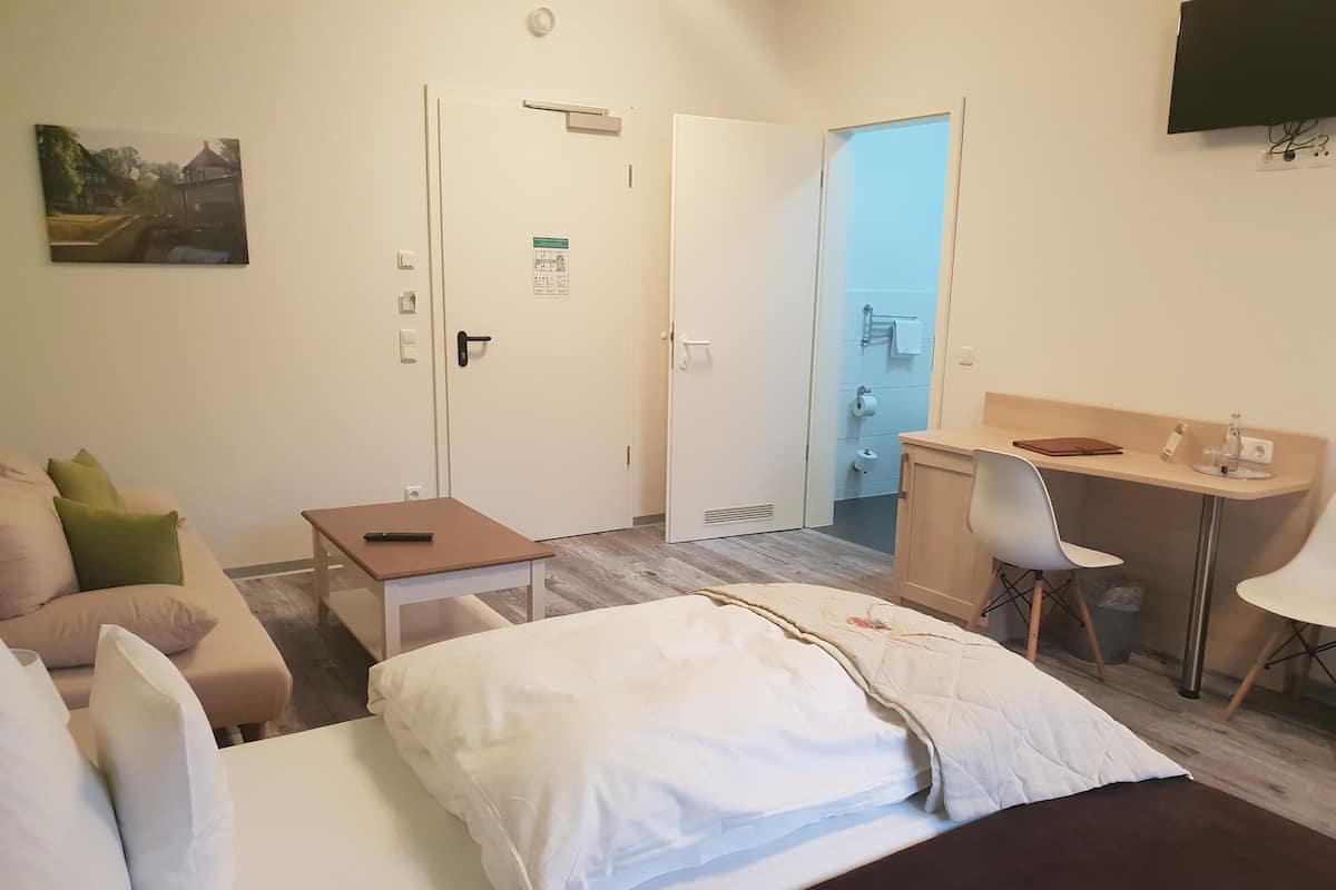 A hotel room with a bed, a desk, a chair, a sofa, and a painting on the wall.