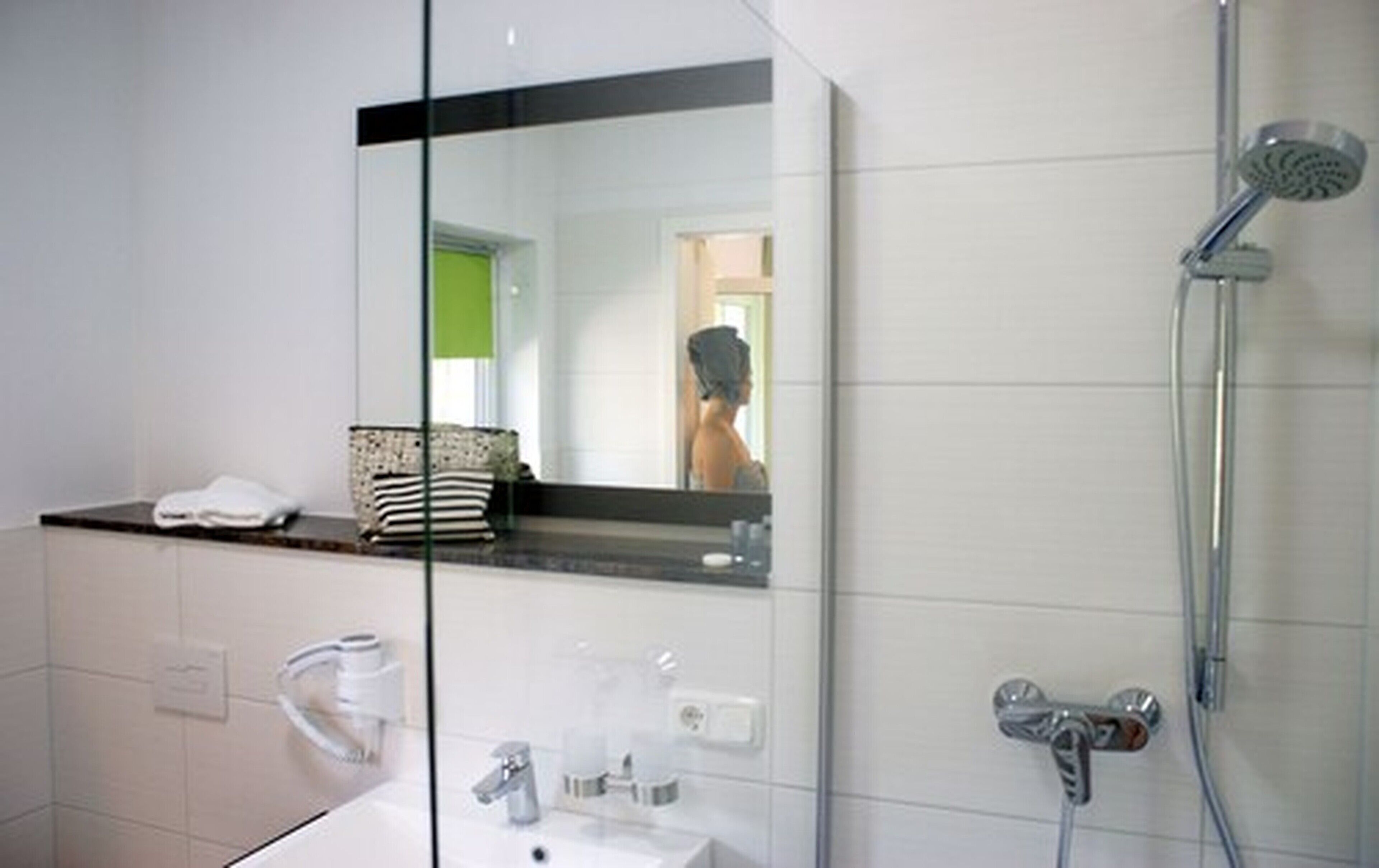 Une salle de bain moderne avec une douche à l’italienne en verre, un lavabo blanc avec un miroir au-dessus, et une serviette posée sur le plan de travail.
