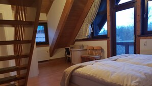 Un dormitorio con una cama, un escritorio y una silla. Hay una ventana que ofrece vistas a árboles y una masa de agua.