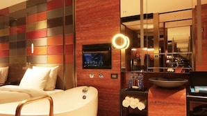 Una habitación de hotel moderna con una bañera grande, un televisor y un espejo con luz.