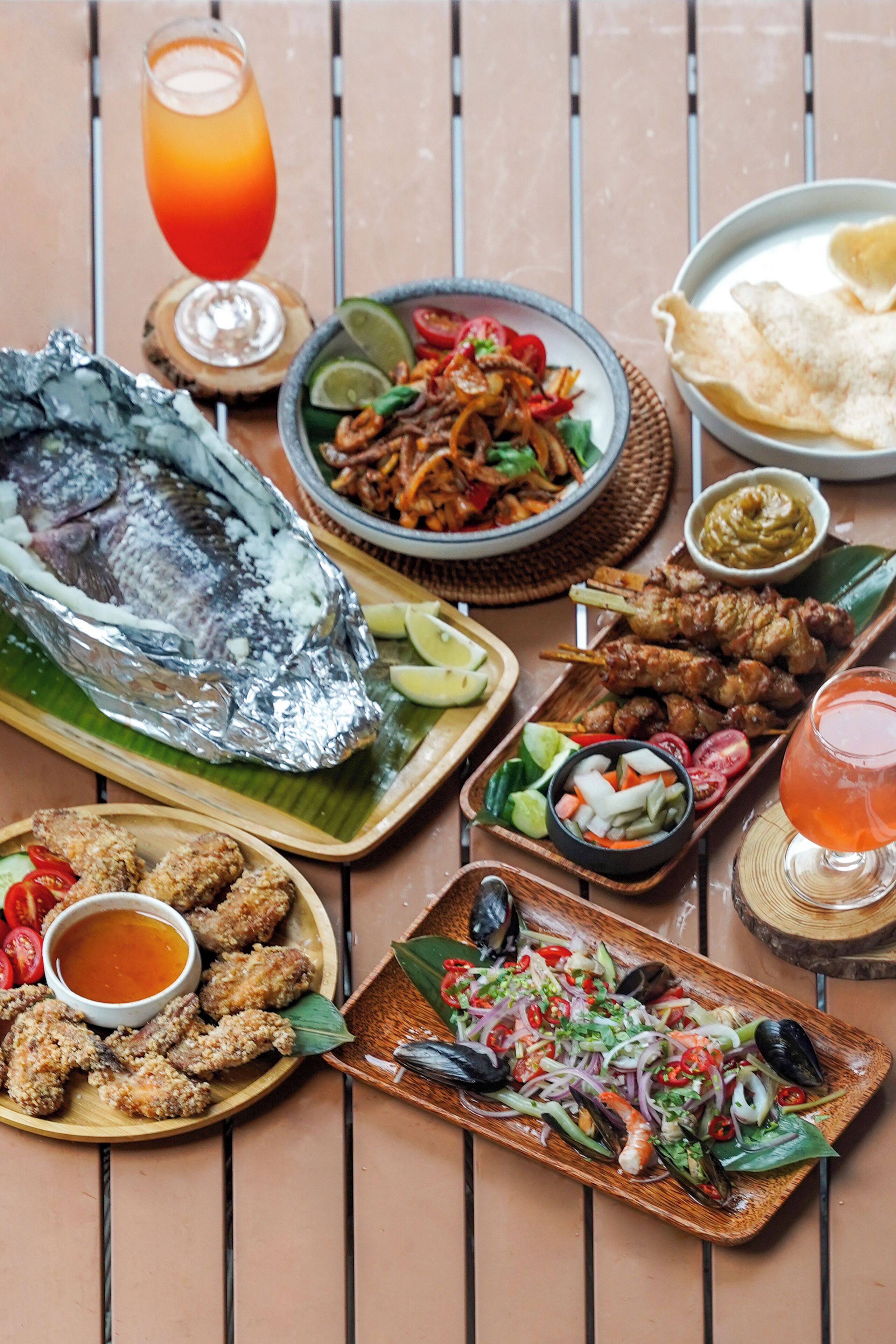 A variety of seafood dishes, a glass of orange juice, and a plate of fried items on a wooden table.