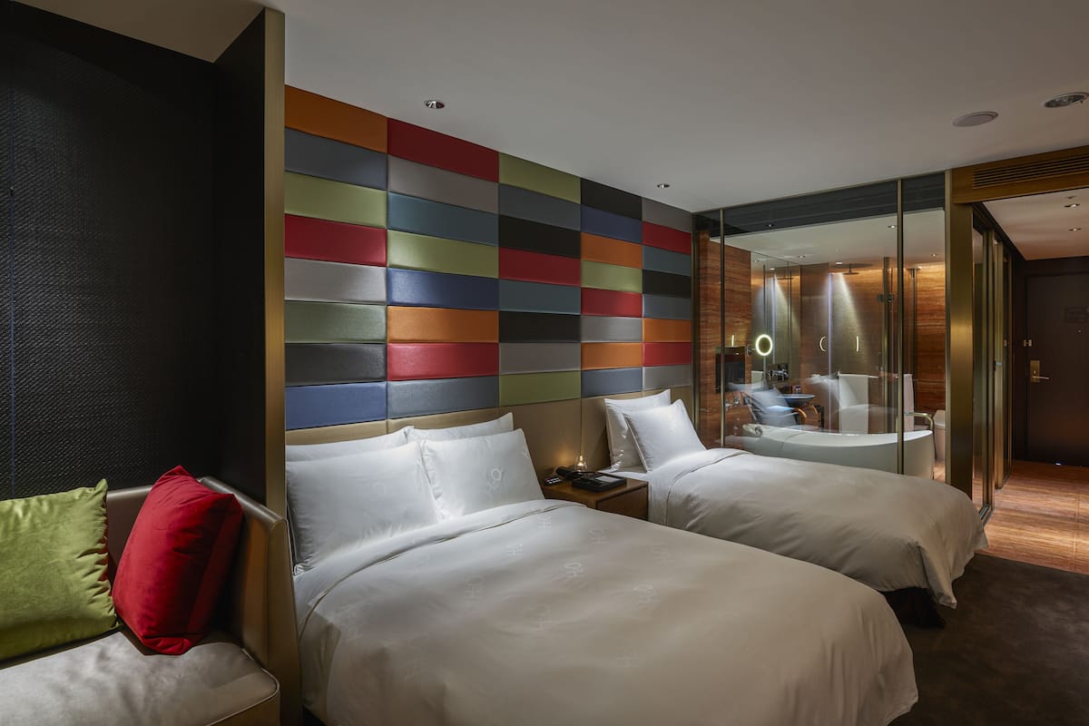 A hotel room with two beds, a large mirror, and a colorful wall panel.