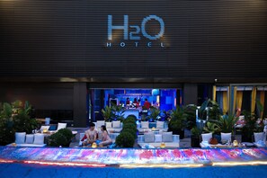 A hotel entrance with a sign reading 'H2O HOTEL,' outdoor seating with cushions and tables, and potted plants. - H2O Hotel (Kaohsiung)