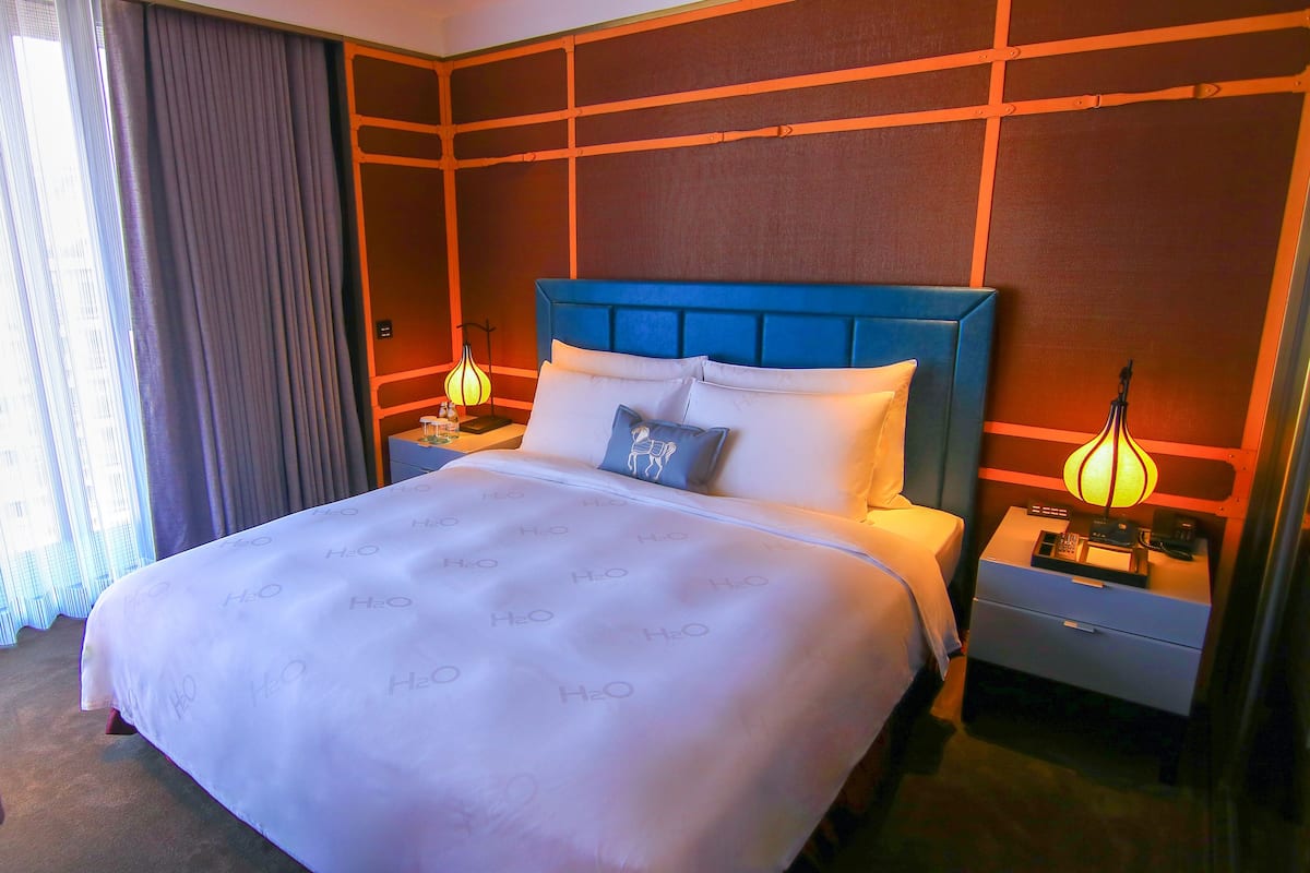 A hotel room with a large bed, two bedside tables with lamps, a TV, and a window with curtains.