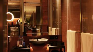 A modern bathroom with a large mirror, a sink, a towel rack, and a small shelf with toiletries.