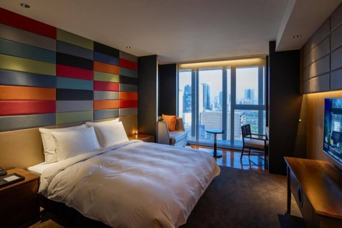 A hotel room with a large bed, a desk, a chair, a TV, and a city view.