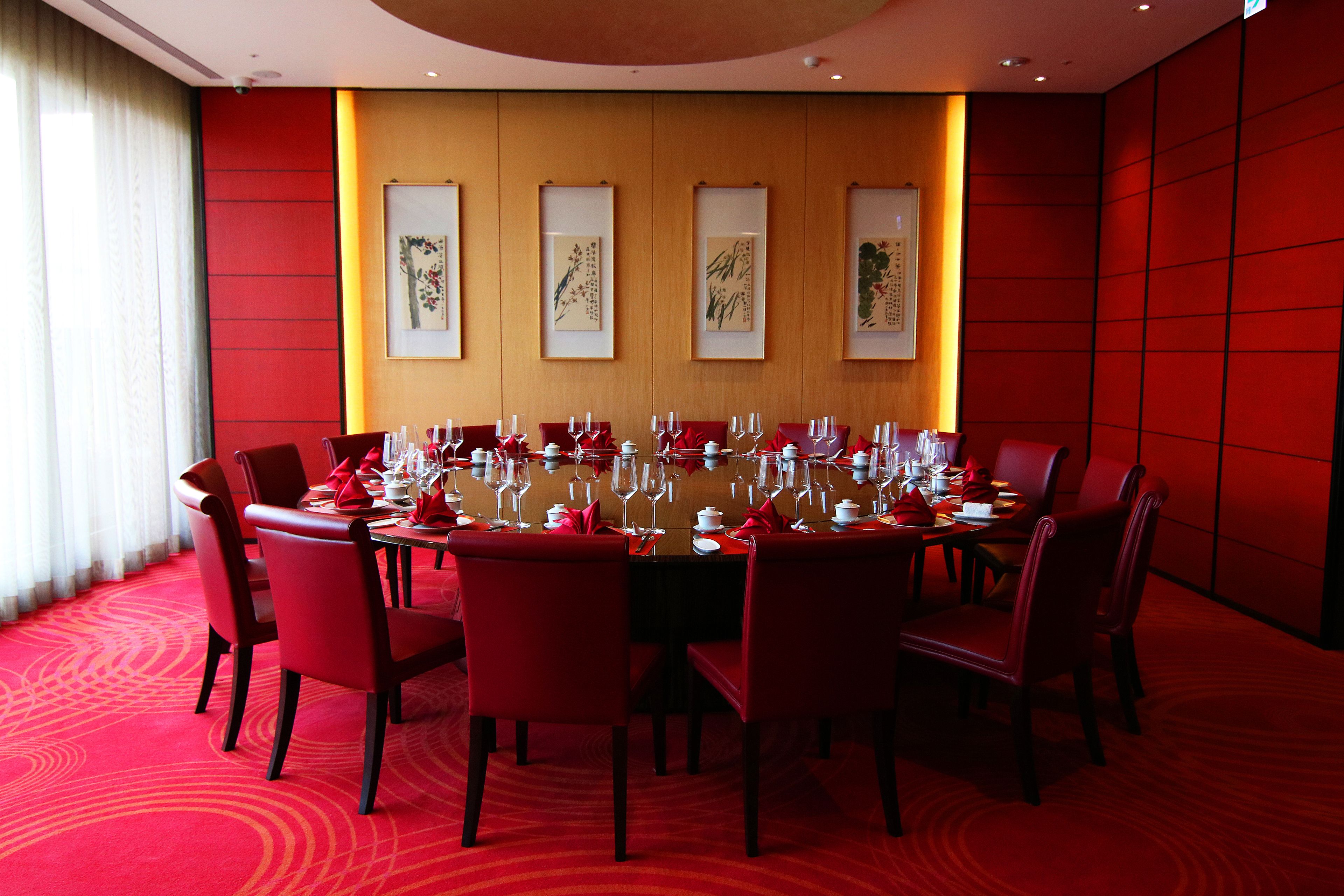 A conference room with a round table, red chairs, and framed artwork on the wall.