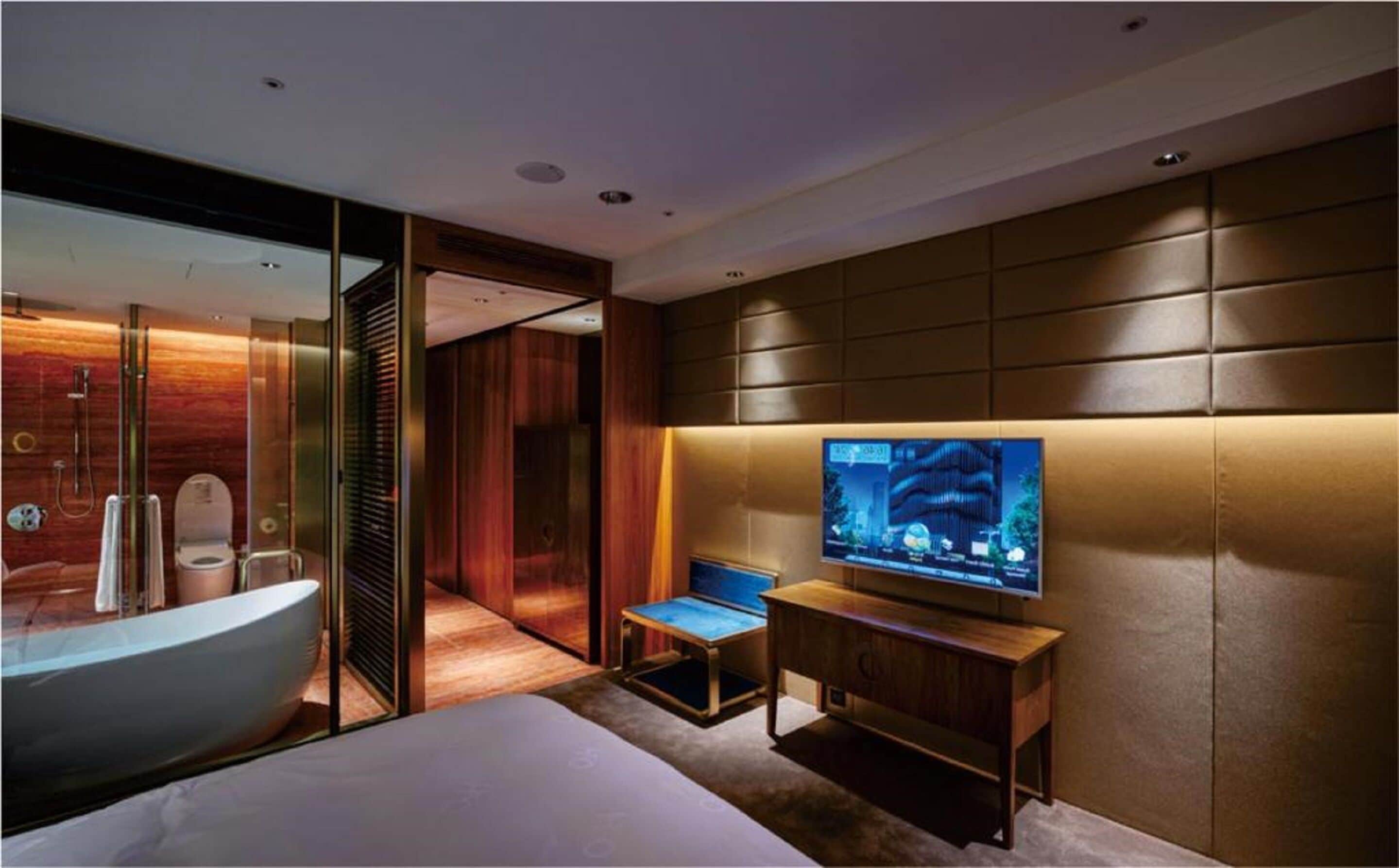 A modern hotel room with a large bed, a television, a small table, and a shower area.