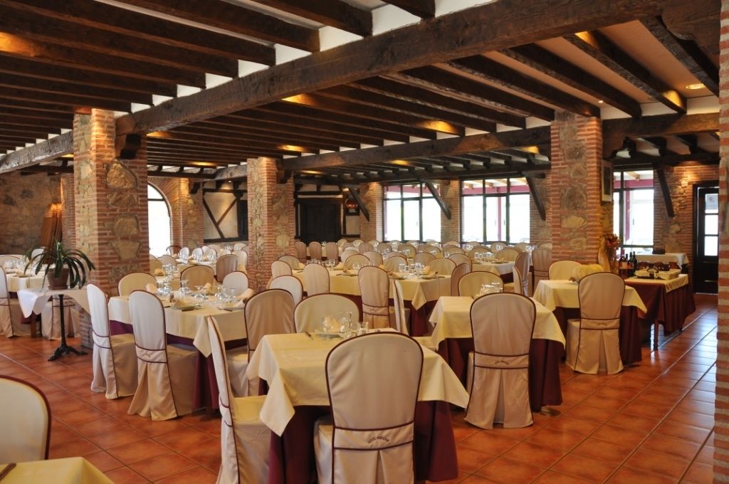 Un salón de banquetes con varias mesas dispuestas para comer, con vigas de madera a la vista y paredes de ladrillo.