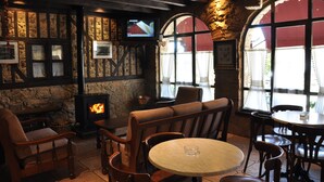 Un restaurant à l’ambiance chaleureuse, avec des murs en pierre, des meubles en bois, une cheminée et de grandes fenêtres.