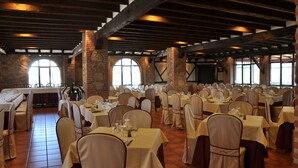 Une salle de banquet avec de nombreuses tables dressées pour le repas, caractérisée par des murs en briques et des poutres en bois.