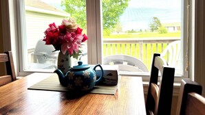 A wooden table with a blue teapot and a vase of flowers by a window. - Jake & Jo's Cottages (Brackley Beach)