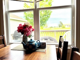 A wooden table with a blue teapot and a vase of flowers by a window.