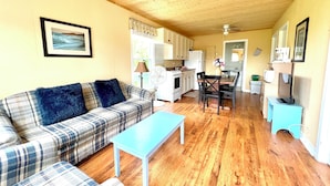 A cozy living room with a plaid sofa, a blue coffee table, and a dining area with a table and chairs. - Jake & Jo's Cottages (Brackley Beach)