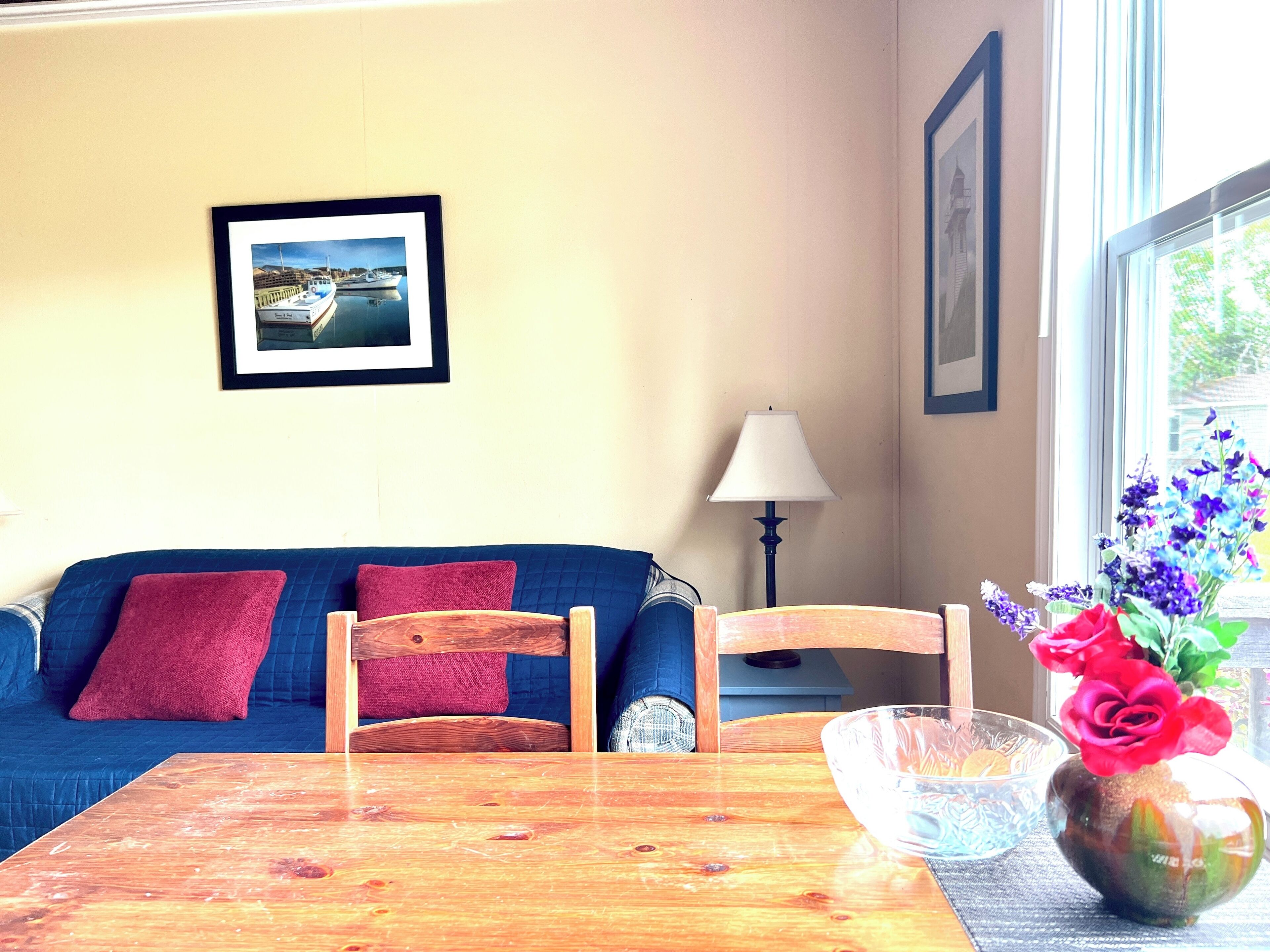 A room with a blue sofa, a wooden table, a vase with flowers, and a framed picture on the wall.