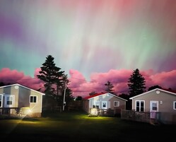 A row of single-story mobile homes with a clear night sky and visible aurora borealis.
