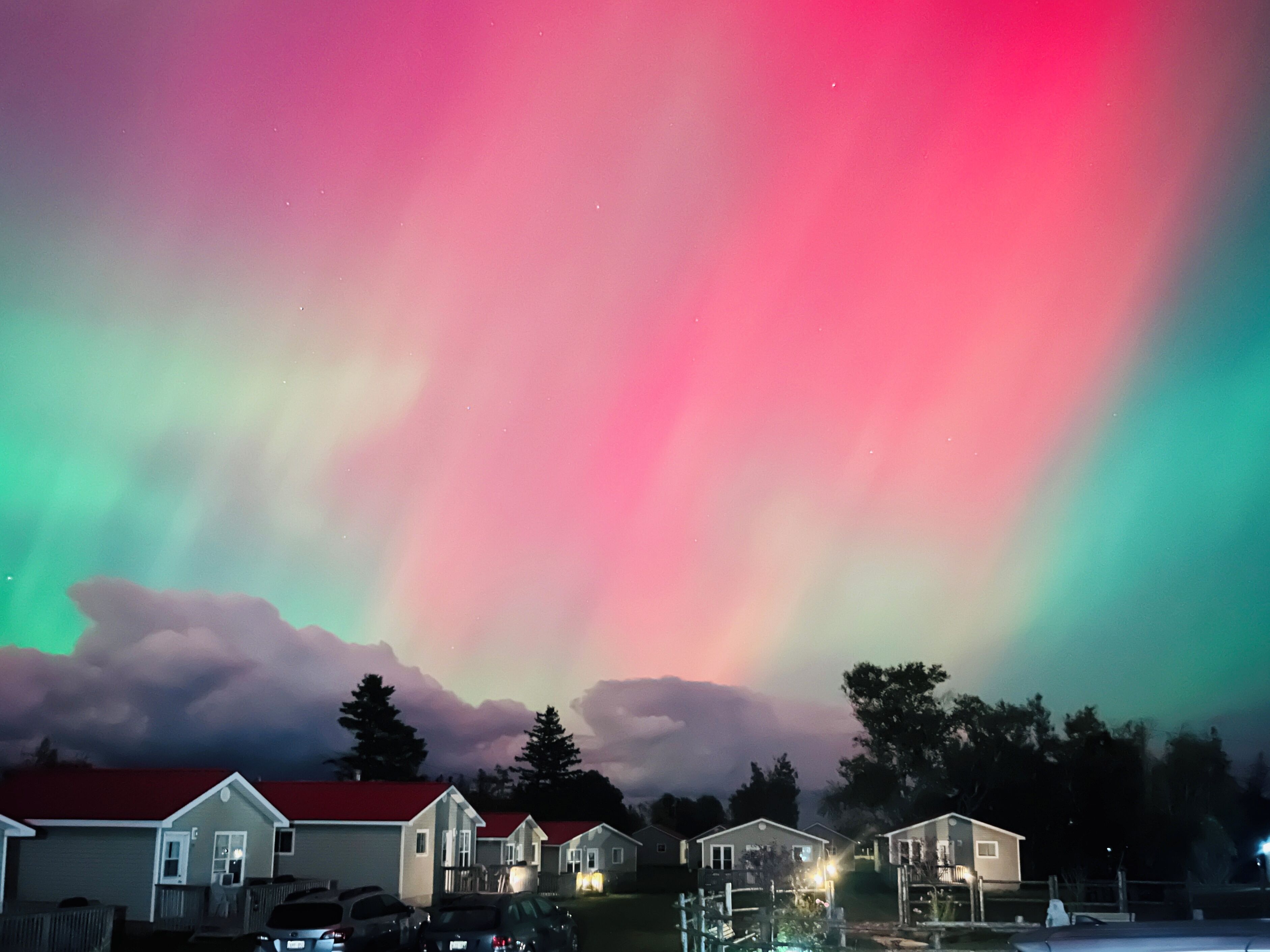 A row of single-story houses with a red roof, under a colorful aurora display.