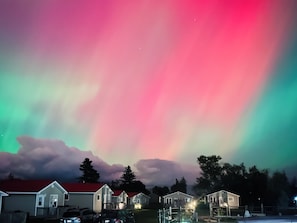 A row of single-story houses with a red roof, under a colorful aurora display. - Jake & Jo's Cottages (Brackley Beach)