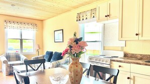 A cozy kitchen with a dining table, chairs, a vase with flowers, and a stove. - Jake & Jo's Cottages (Brackley Beach)