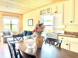 A cozy kitchen with a dining table, chairs, a vase with flowers, and a stove.