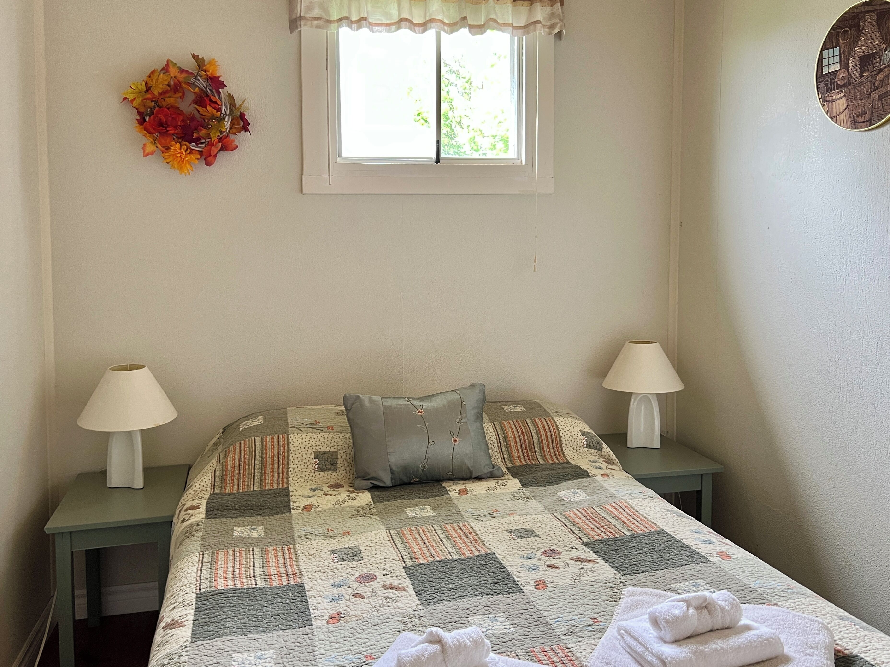 Un dormitorio con colcha acolchada, dos lámparas de noche, una ventana con vistas y una decoración en la pared.