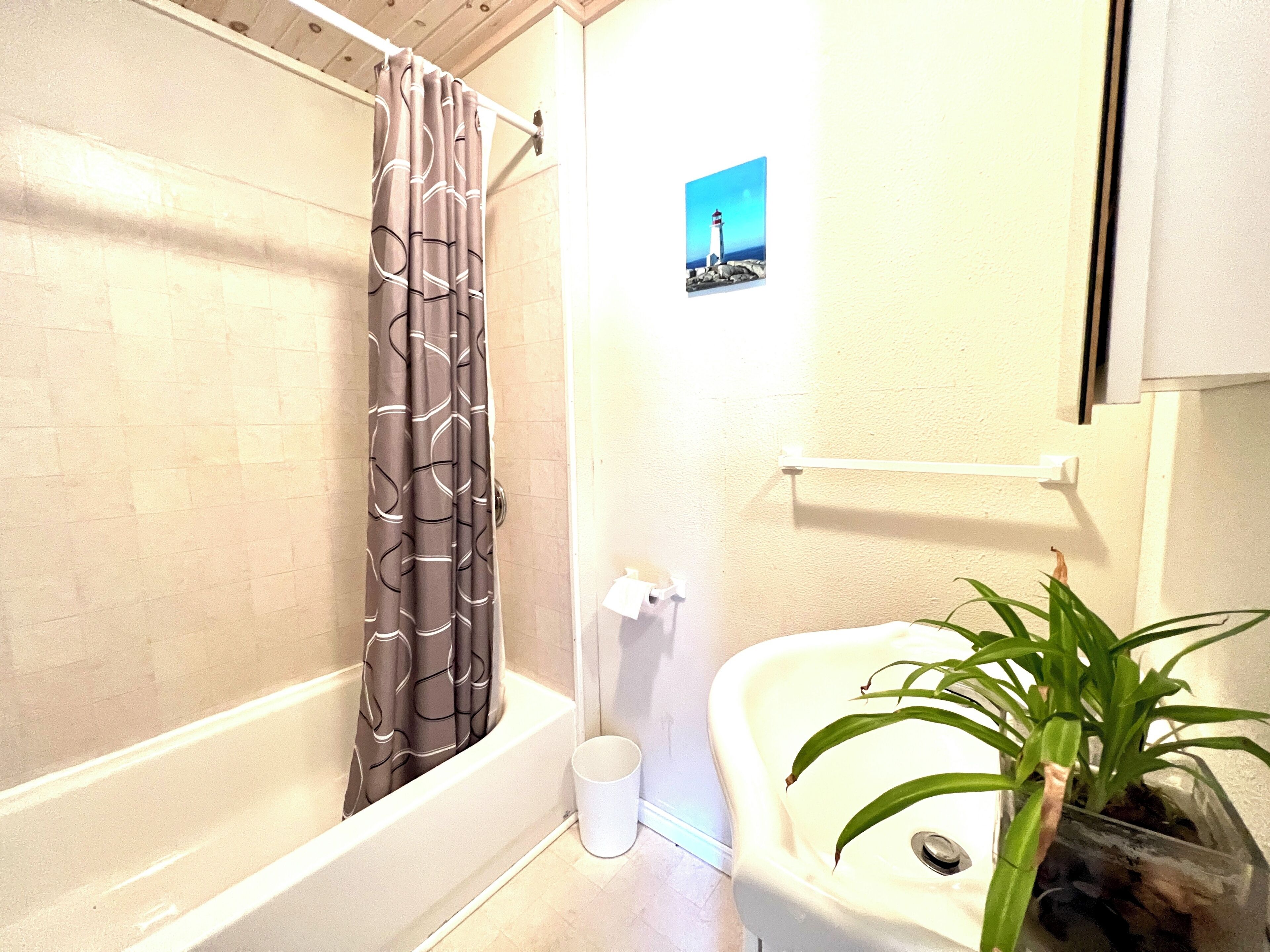 Un baño con bañera, lavamanos, una planta en maceta y un cuadro en la pared.