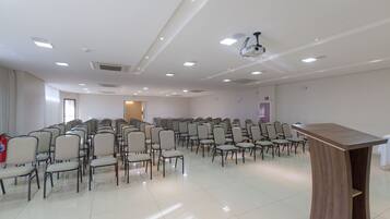 A conference room with rows of chairs, a podium, and a projector on the ceiling.