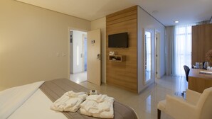 Una habitación de hotel moderna con una cama, un escritorio, una silla, un televisor y un baño visible a través de una puerta abierta.