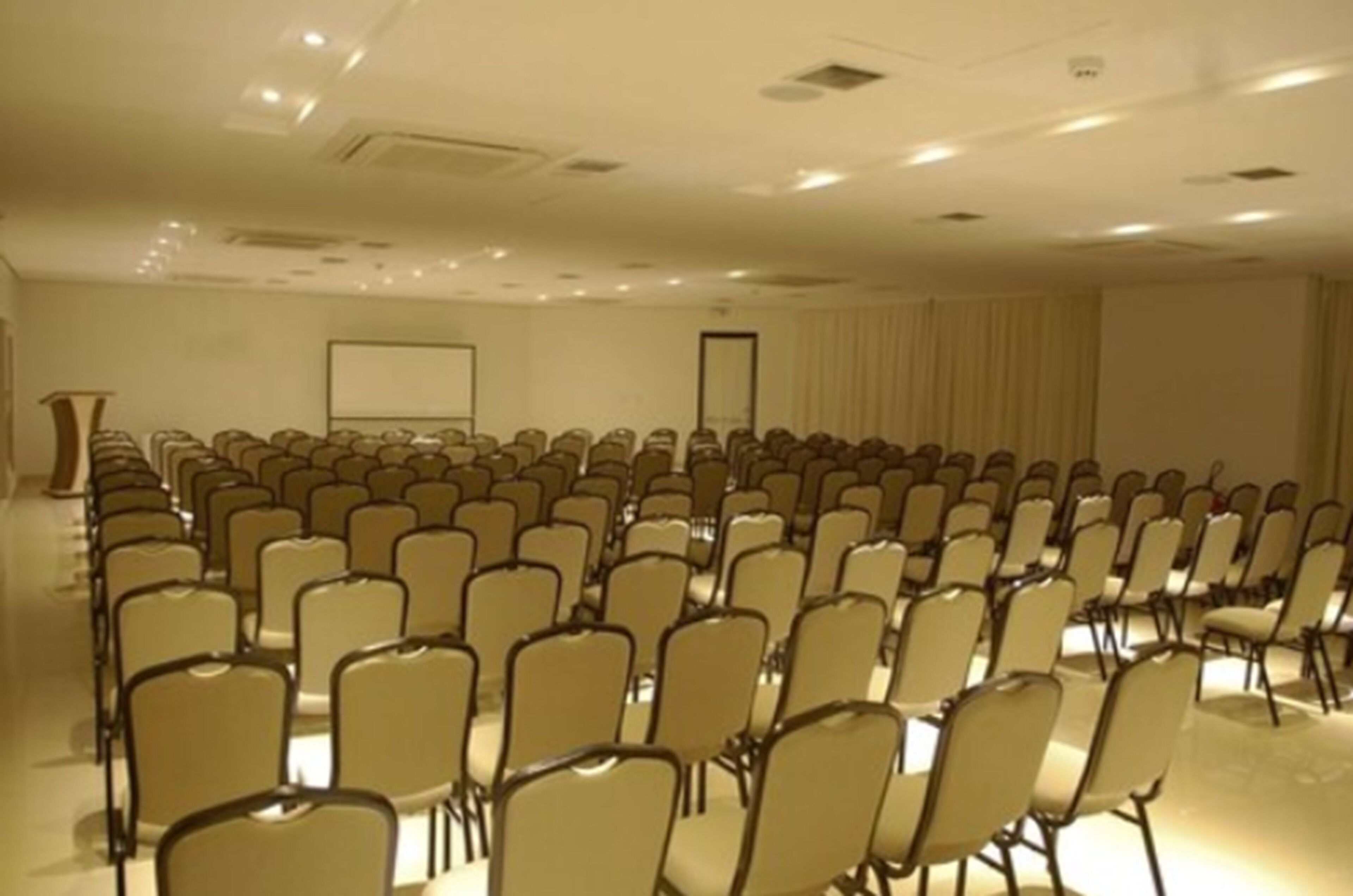 A conference room with rows of chairs, a podium, and a projection screen.