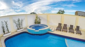 Una piscina con jacuzzi, rodeada de sillas de descanso y plantas en macetas.