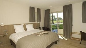 A modern bedroom with a large bed, a nightstand, a chair, and a view of a garden through a sliding glass door.