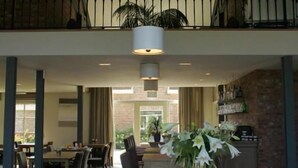 A spacious lobby with a high ceiling, a central table with books and a vase of flowers, and a staircase leading to an upper level.