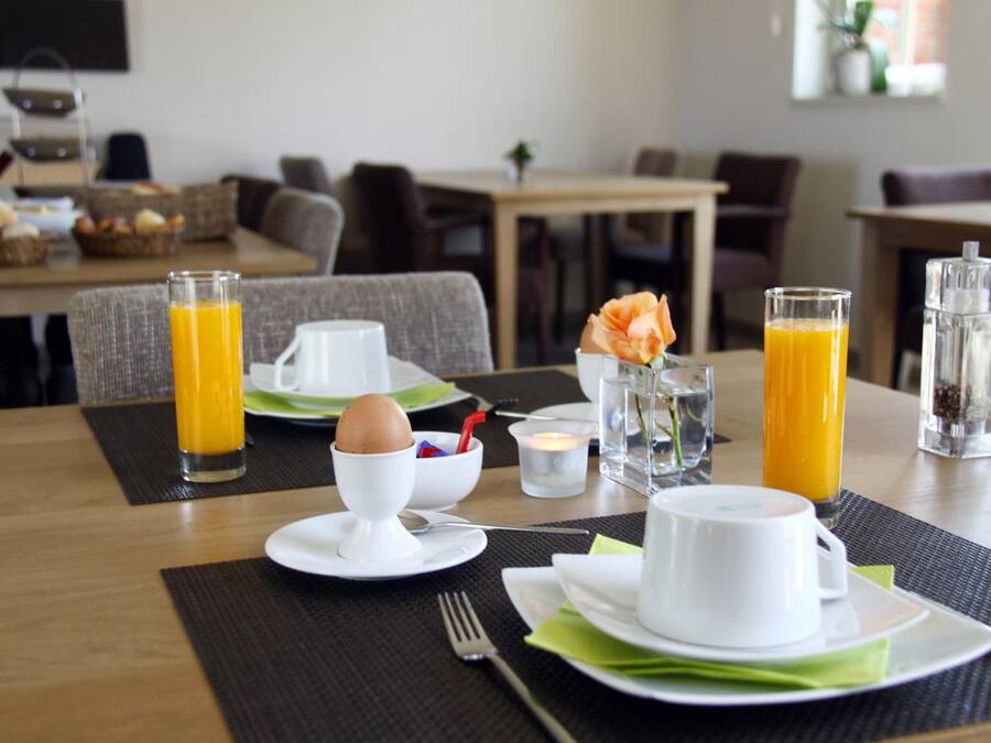 A breakfast setting with a table set for two, including plates, cups, a glass of orange juice, a glass of water, and a candle.