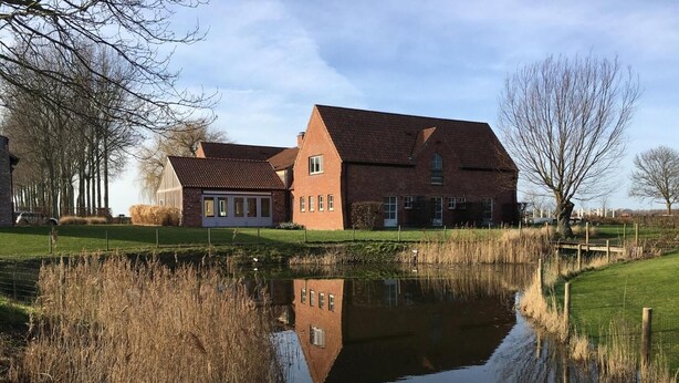 A large brick building with a pond in front, surrounded by trees and grass.