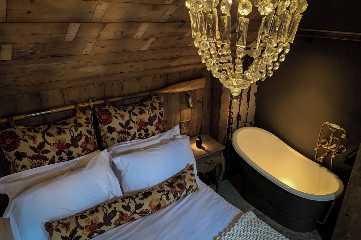 Une pièce en bois avec un lit, un lustre et une baignoire.