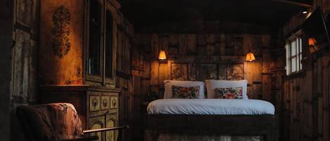 A rustic bedroom with a wooden headboard, a large bed with floral pillows, a wooden dresser, and a chandelier.