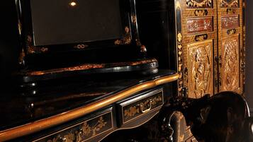 A dark wooden desk with a mirror, a chair, and a decorative cabinet with intricate carvings.